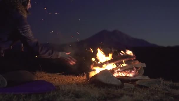 Молода кемпінгова жінка, сидячи, кидає деревину в палаючий вогонь, повільний мо — стокове відео