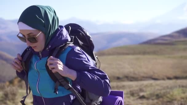 Linda mulher muçulmana turista com mochila e óculos de sol viaja em belas montanhas, slow mo — Vídeo de Stock