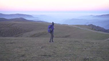 Kadın turist sırt üstünde onun sırt çantası ile dağlarda akşam yayılıyor.