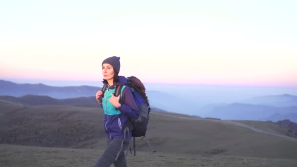 Turista mujer con mochila viaja al atardecer en las montañas de fondo — Vídeo de stock