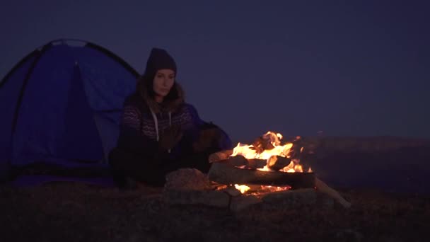 Mulher acampar à noite sentado perto da tenda e se saciando ao lado do fogo, slow mo — Vídeo de Stock