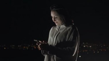 Rüzgar gece şehrin arka plan üstünde a telefon ile şık bir kız portresi