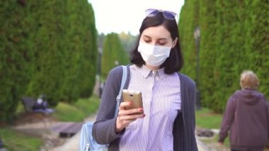 Kullanarak telefon, yavaş mo parkta yüzünde koruyucu tıbbi maskeli güzel kız