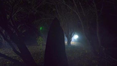 bir şekil bir mum ile siyah bir elbise içinde gizemli bir orman geçer