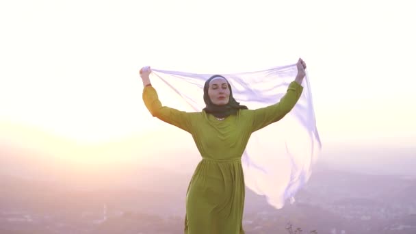 Muslimská dívka v látku v rukou, na okraji útesu, západ slunce — Stock video