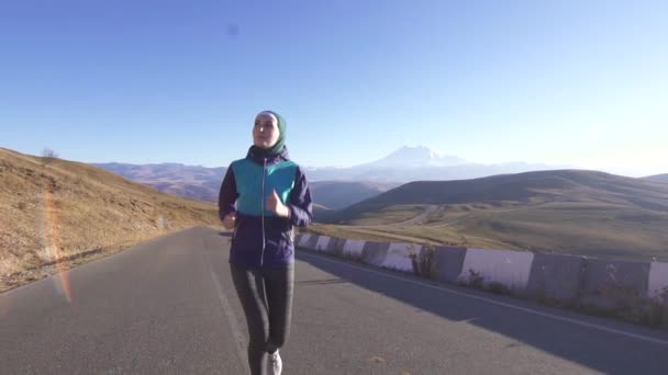 Sportos fiatal muzulmán nő egy sálat, napos hegyi úton, lassú mo — Stock videók