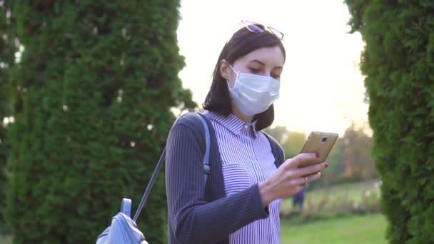 Meisje in een beschermende medische masker op haar gezicht gaat en maakt gebruik van de telefoon, de langzame mo — Stockvideo