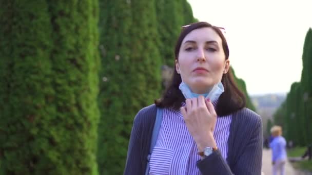 Dívka sundá masku lékařské z jejího obličeje a hluboce inhaluje vzduchu v parku — Stock video