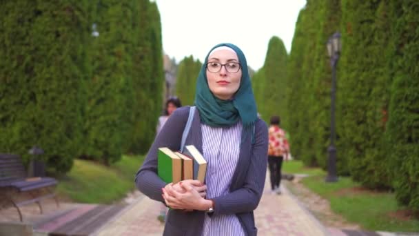 Арабский студент в хиджабе с книгами идет в парк учиться — стоковое видео