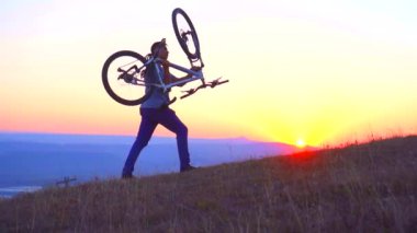 Adam bir bisiklet dağ günbatımı, yavaş mo, taşır.
