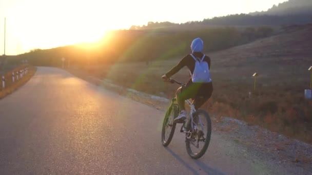 Donna musulmana in hijab con zaino in sella a una bicicletta sul sole che tramonta, vista posteriore — Video Stock