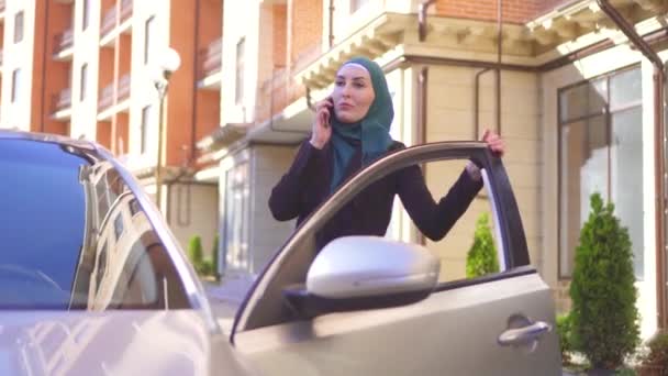 Mulher muçulmana em hijab falando ao telefone e senta-se no carro — Vídeo de Stock