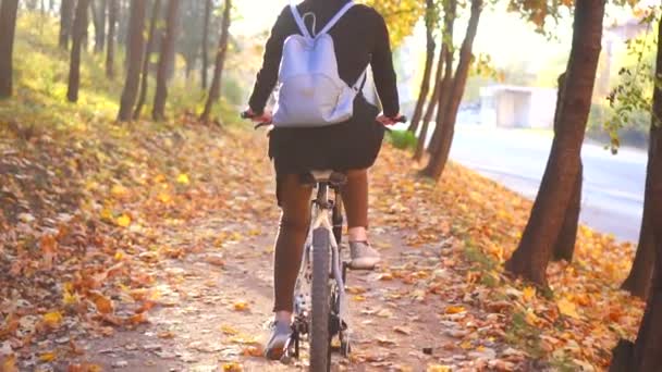 Muslim woman in a hijab and with a backpack on her back rides a bicycle in autumn park rear view,slow mo — Stock Video