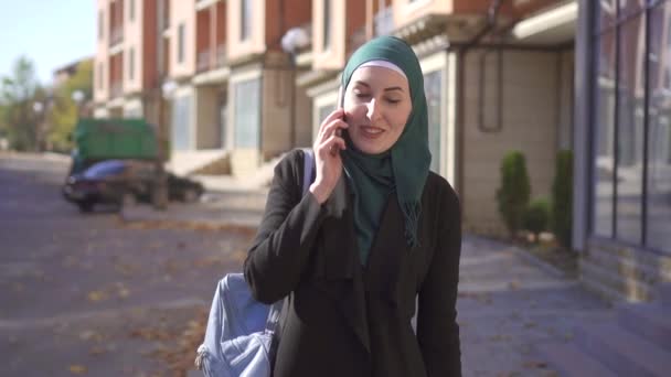 Mujer musulmana en hiyab caminando y hablando por teléfono en la ciudad, lento mo — Vídeo de stock