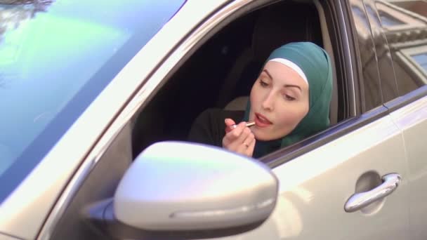 Μουσουλμανική γυναίκα σε ένα hijab κάθεται σε ένα αυτοκίνητο και να χρωματίζει τα χείλη με κραγιόν, αργή mo — Αρχείο Βίντεο