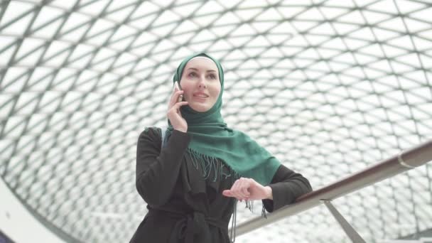 Bir sırt çantası ile bir hijab oldukça Müslüman kadında bir alışveriş merkezinde duruyor ve telefonda konuşurken, yavaş mo — Stok video