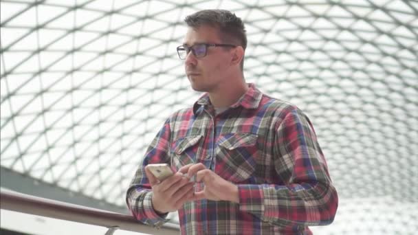 Retrato hombre con gafas se encuentra en un centro comercial y utiliza el teléfono, mo lento — Vídeos de Stock