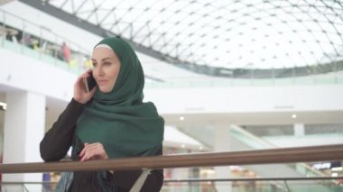 Bir sırt çantası ile bir hijab oldukça Müslüman kadında bir alışveriş merkezinde duran ve telefonda konuşurken
