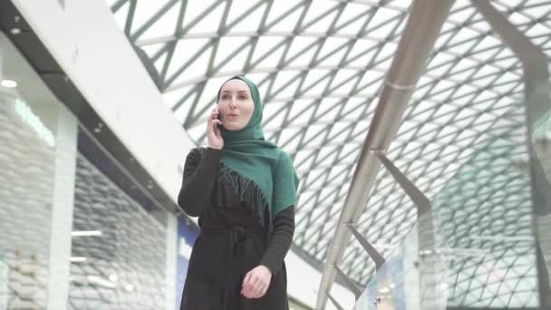 Mujer bastante musulmana en un hijab con una mochila va al centro comercial y habla por teléfono, lento mo — Vídeos de Stock