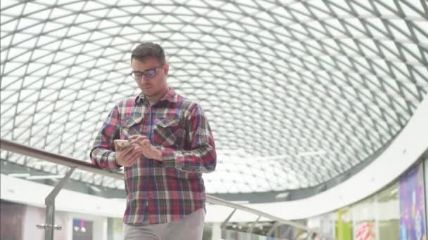 Mann mit Brille steht in Einkaufszentrum und telefoniert langsam — Stockvideo