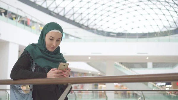 美丽的穆斯林女孩在头巾使用智能手机在现代商务中心 — 图库照片