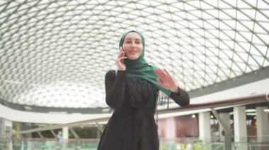 Bir sırt çantası ile bir hijab oldukça Müslüman kadında bir alışveriş merkezinde duran ve telefonda konuşurken
