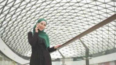 Bir sırt çantası ile bir hijab oldukça Müslüman kadın alışveriş merkezine gider ve telefonda konuşuyor