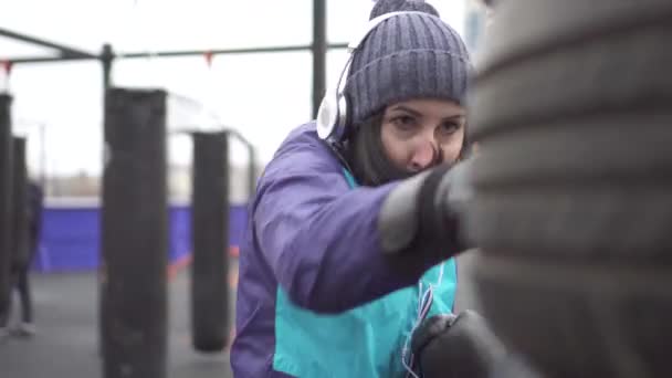 Mulher atleta em luvas de boxe bate uma pêra em um chão de treinamento de rua, close-up — Vídeo de Stock
