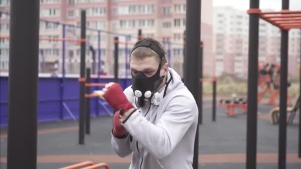 Homme dans un masque d'entraînement sur son visage boxe sur une aire de jeux de rue sportive, lent mo — Video