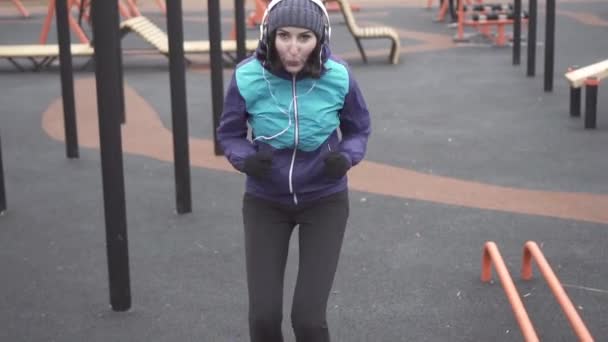Женщина-спортсмен в наушниках делает тренировку на улице детская площадка, медленное мо — стоковое видео