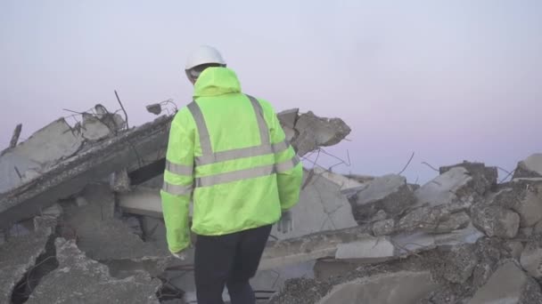 A rescuer in a signal vest after an earthquake sneaks around a destroyed house — Stock Video