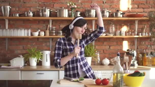Jeune femme dans les écouteurs prépare et danse dans la cuisine — Video
