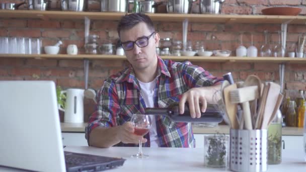 Soltero solitario en la cocina bebiendo vino y mirando un portátil blanco — Vídeo de stock