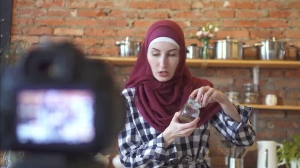 Muslim woman in hijab blogger in the kitchen in front of the camera talks about cooking — Stock Video