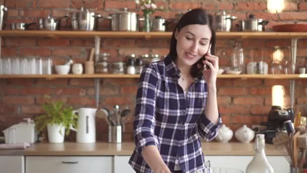Женщина разговаривает по телефону и готовит на кухне режет огурец — стоковое видео