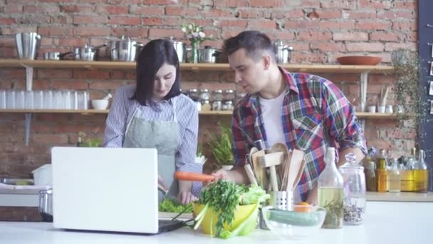 Ein Mann und eine Frau bereiten in der Küche eine Videostunde vor, während sie sie auf einem weißen Laptop ansehen — Stockvideo