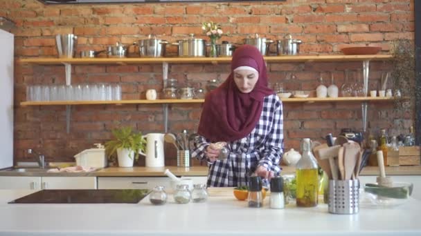 Mujer joven musulmana en hiyab corta verduras y usa condimentos en la cocina — Vídeo de stock