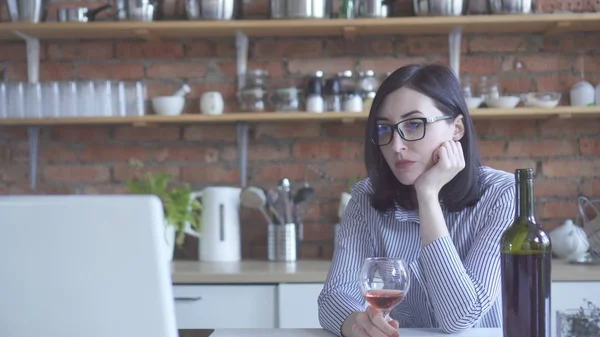 lonely woman business woman drinks wine in the kitchen looking at a laptop