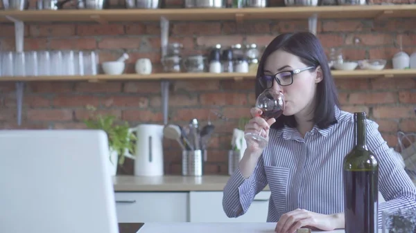 Stylish girl in glasses drinks from a glass of wine in the kitchen at home — Stock Photo, Image