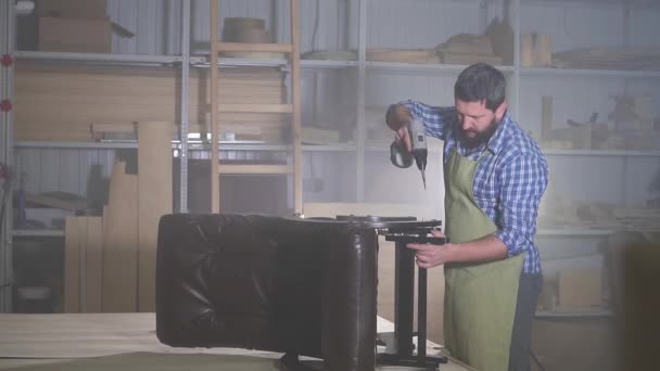 El hombre profesional con la barba en la camisa se dedica a la colocación de la sujeción de la silla de muebles en el taller oscuro — Vídeo de stock