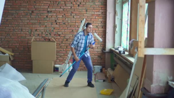 Expressive cheerful man in shirt and headphones sings and dances during repairs — Stock Video