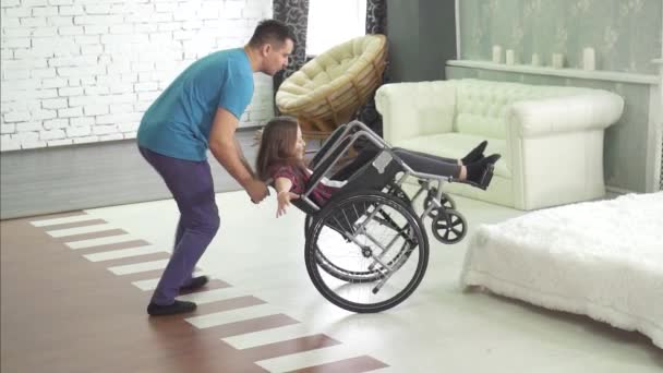 Niño discapacitado alegre en una silla de ruedas en casa con su padre — Vídeos de Stock