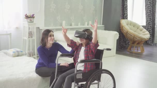 Adolescente deficiente em uma cadeira de rodas e sua mãe em casa usando a tecnologia vr — Vídeo de Stock