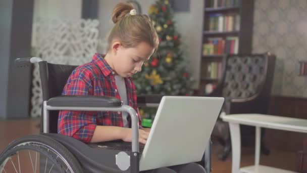 在轮椅上残疾的少女, 坐在笔记本电脑上, 靠在圣诞树上 — 图库视频影像