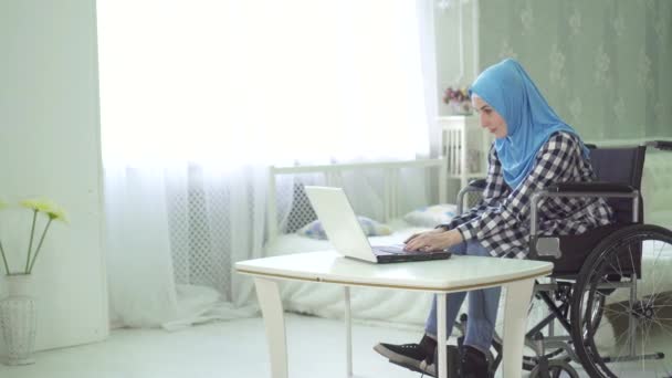 Hermosa joven en hijab persona con discapacidad, silla de ruedas, trabajo en la computadora — Vídeos de Stock
