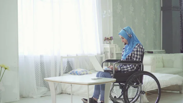 Красивая молодая женщина в хиджабе, улыбающийся инвалид, инвалидная коляска, удаленная работа в Интернете — стоковое фото