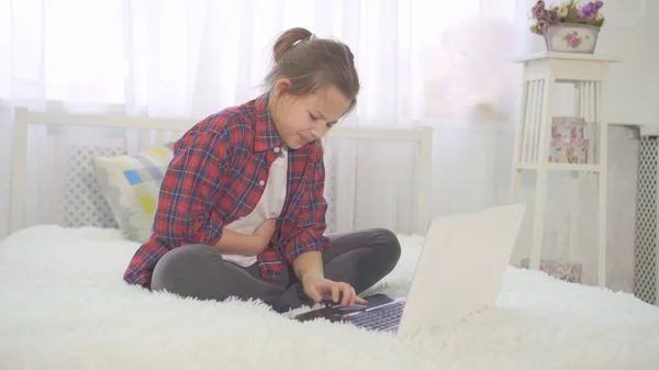 bir dizüstü bilgisayar ile bir yatakta evde oturan bir genç kız olarak şiddetli karın ağrısı