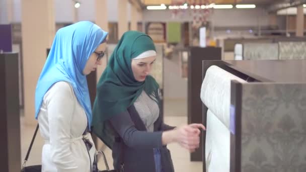 Dos mujeres musulmanas jóvenes en la tienda de mejoras para el hogar elegir el papel pintado — Vídeos de Stock