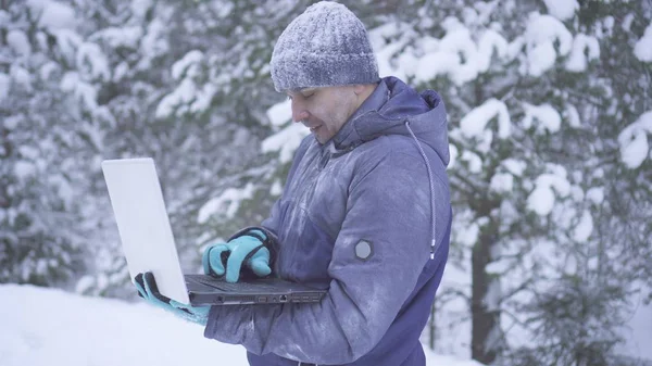 Portrait frozen man in winter forest uses laptop — Stok fotoğraf