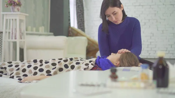 La niña en la cama tiene un resfriado en casa, una tos fuerte, comprobando la temperatura de su madre — Foto de Stock